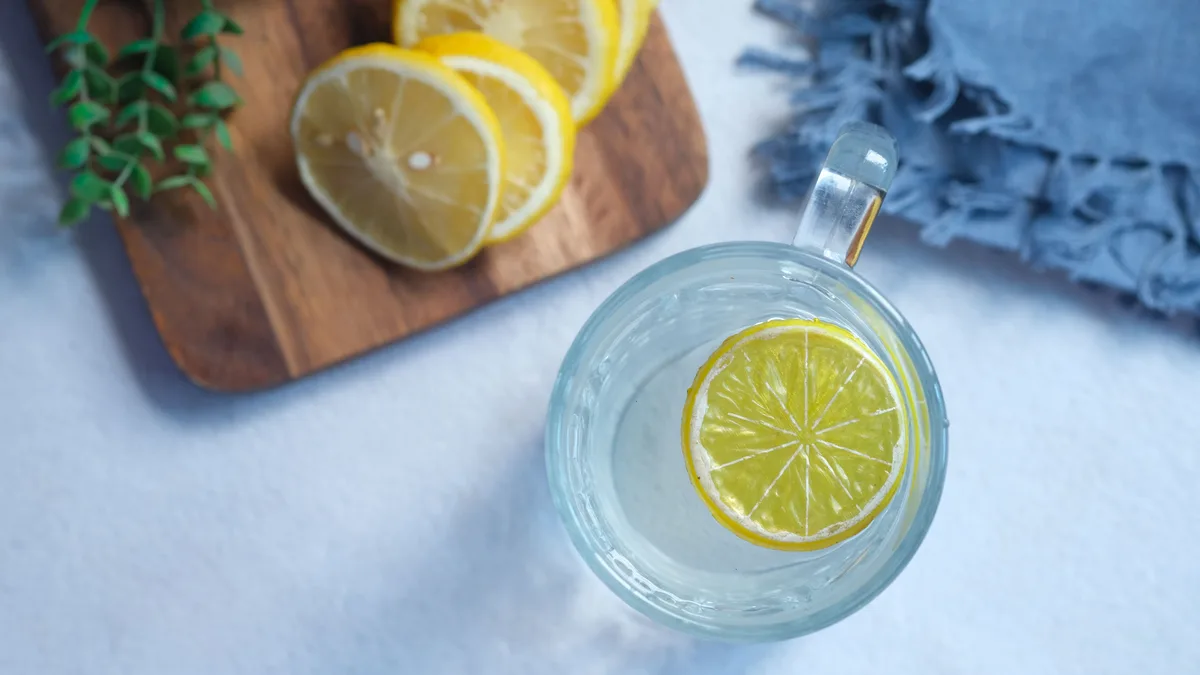 Mavi bezin üzerinde limon dilimli bir bardak su, yanında kesilmiş limonlar
